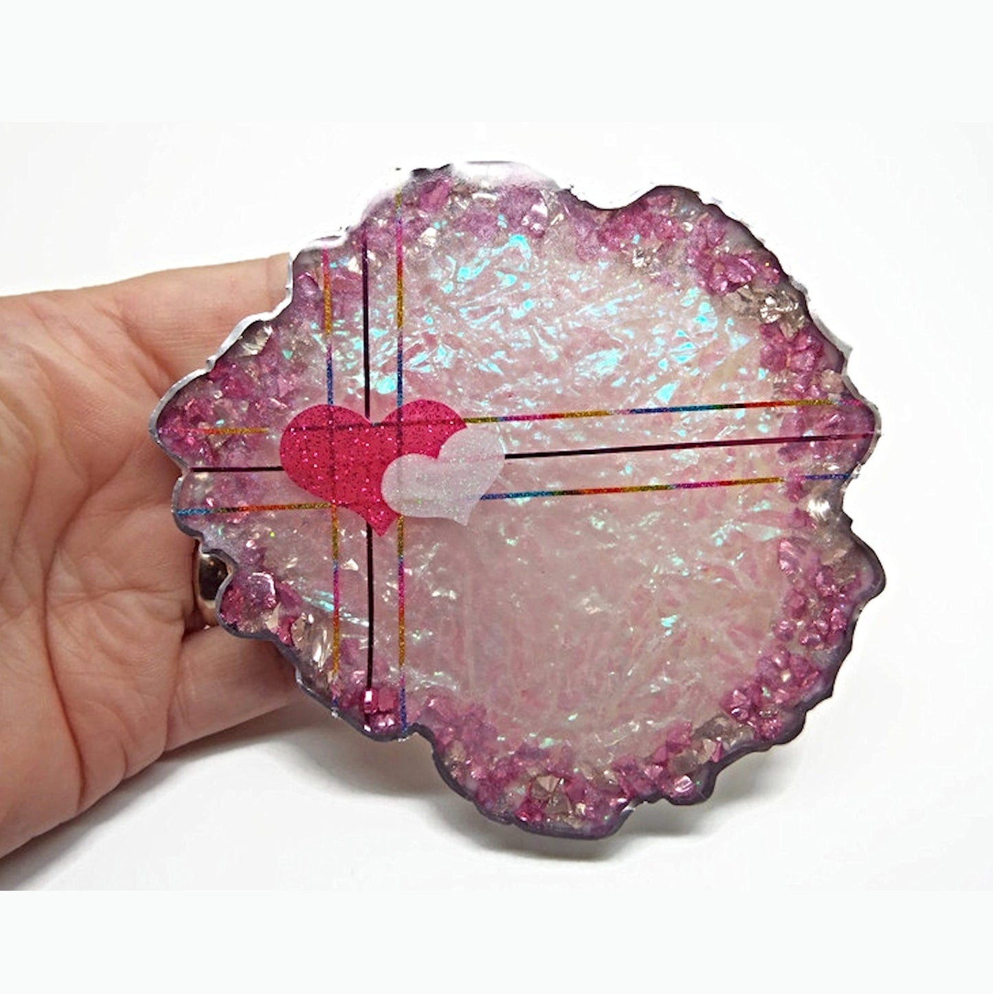 Hand holding a round geode shaped resin coaster in pink with two hearts and coloured stripes